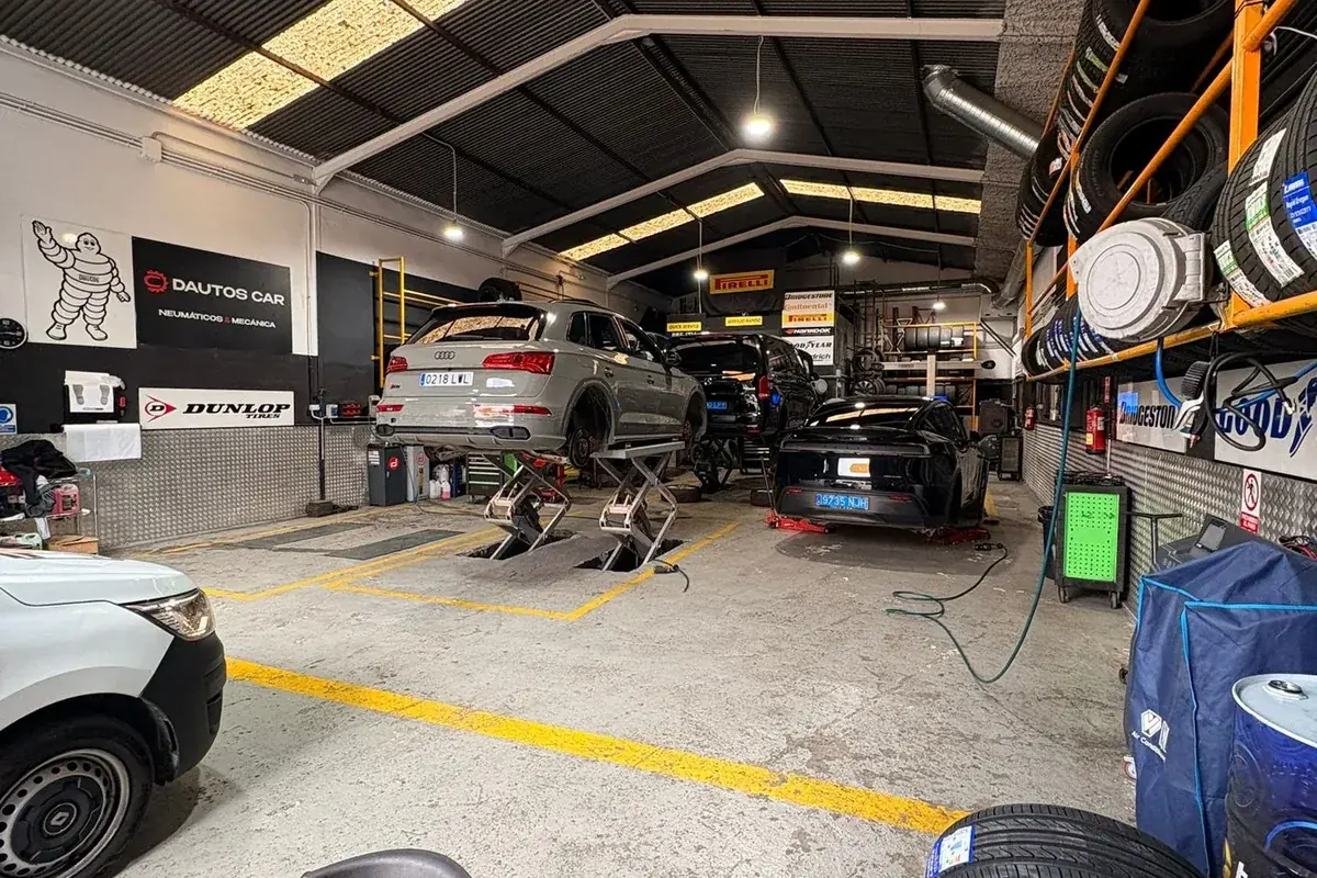 Coche elevado con la rueda desmontada y los neumáticos retirados en el suelo del taller Dautos Car de Marbella